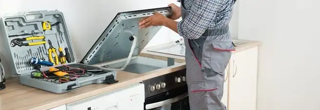 Cooktop repair technician lifting a built-in stovetop for service in Columbus, GA