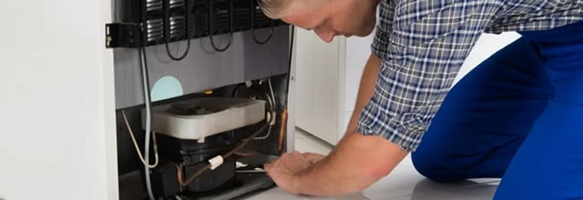 Refrigerator repair technician servicing the compressor and condenser area in Columbus, GA