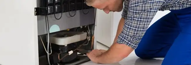 Refrigerator repair technician servicing the compressor and condenser area in Columbus, GA