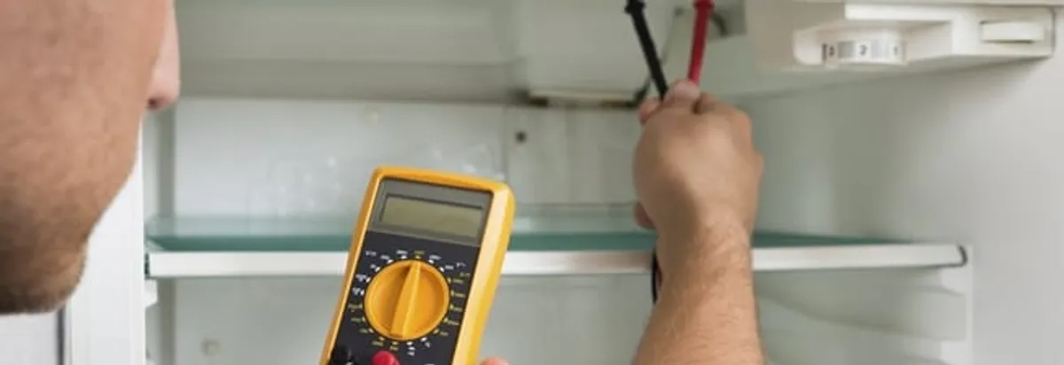 Refrigerator repair technician testing electrical components with a multimeter in Columbus, GA