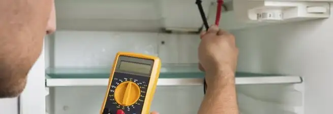 Refrigerator repair technician testing electrical components with a multimeter in Columbus, GA
