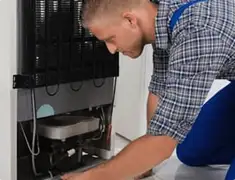 Refrigerator repair technician servicing the compressor and condenser area in Columbus, GA